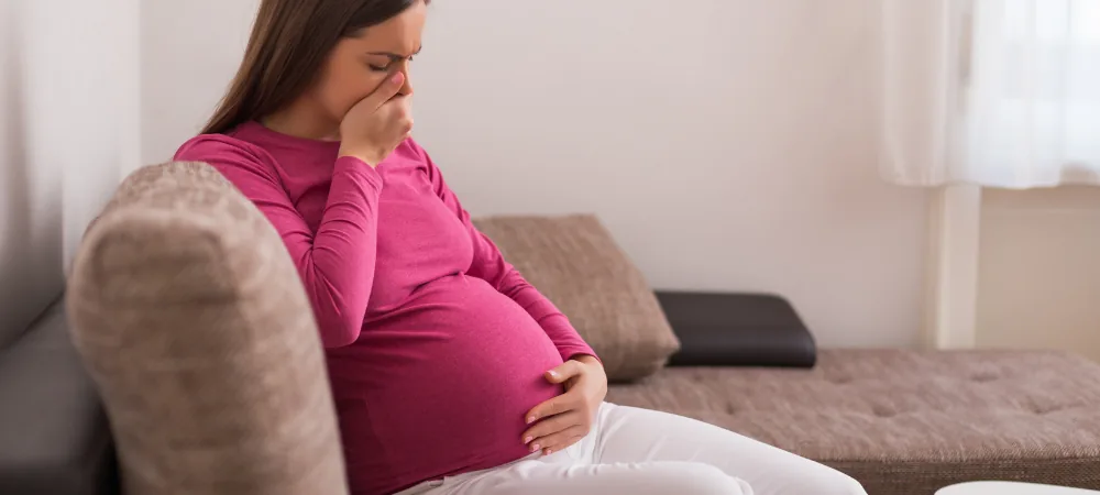 Pregnant woman suffering from nausea, sitting on a sofa